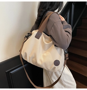 Detail of canvas tote bag showing dark brown fabric handle and leather logo patch
