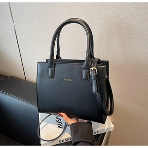 Close-up of black matte leather tote with golden logo and adjustable shoulder strap