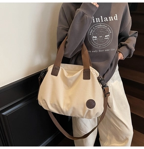 Detail of a large canvas tote bag with brown straps and logo patch shown on a model