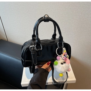 Detail of black glossy leather bowling bag with soft plush ball and heart charm