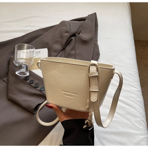 Détail du sac seau crème en cuir plissé avec nœud décoratif et logo de la marque