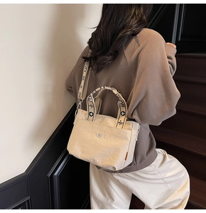 Detail der beigen Segeltuchtasche mit geometrischem Jacquard-Gurt und Metalllogo