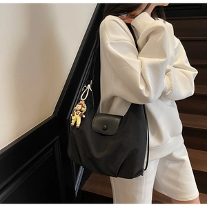 Close-up of black canvas tote bag with leather flap and cute yellow doll pendant detail