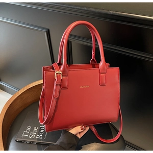 Detail of red structured crossbody handbag with gold branding and adjustable shoulder strap
