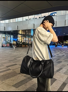 Black leather duffel bag with geometric texture shown on shoulder in urban city setting
