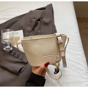 Détail du sac seau crème avec texture plissée, bandoulière et pendentif en cœur