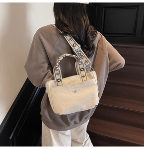 Detail der cremeweißen Canvas-Tasche mit Silberbeschlägen und breitem Logo-Schultergurt