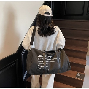 Lifestyle view of a large black canvas travel tote bag with shoulder strap on stairs