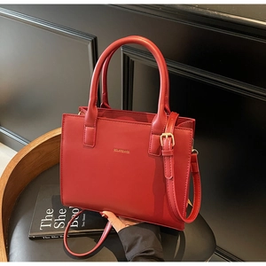 Detail of red leather tote bag showing golden logo text and adjustable shoulder strap