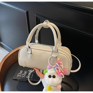 Detail of a creamy white bowling bag with a colorful plush monster charm on dark background