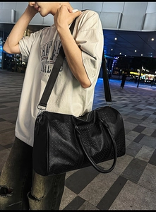 Detail of black woven texture travel bag with adjustable strap on a male model
