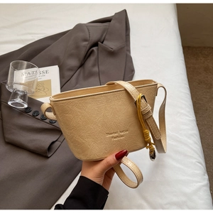 Vue détaillée du sac seau beige en cuir plissé avec bandoulière dans un décor cosy