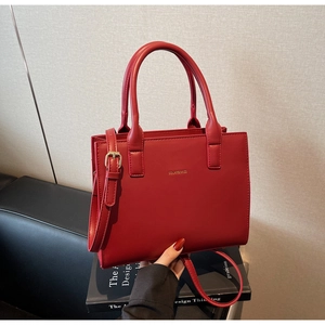 Close-up of red leather handbag featuring gold logo and round handle on black book