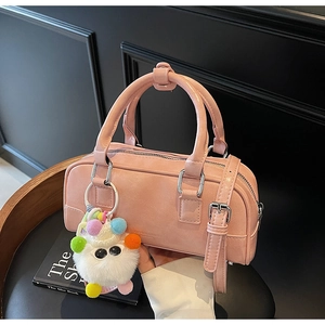 Pink bowling bag detail with plush monster charm and silver hardware on a leather chair
