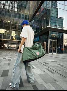 Outdoor shot of a large dark green nylon tote bag with black straps and shoulder strap
