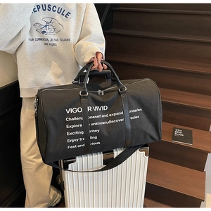 Black canvas travel tote bag with leather handles shown beside a white suitcase on stairs