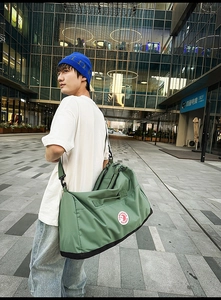 Close-up of a large green nylon tote bag with wide black strap in an urban outdoor setting