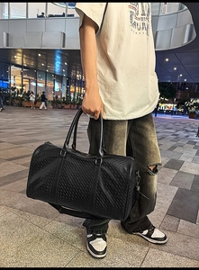 Detail of black cylindrical PU leather travel tote featuring unique diagonal stitched textures