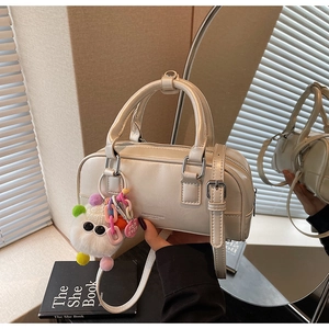 Detail of cream Boston bag with leather texture, logo embossing and plush monster charm
