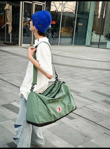 Outdoor street shot of large green nylon travel bag with shoulder strap and brand logo