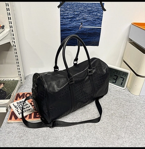 Close-up of embossed black leather travel tote showing handles and wide shoulder strap