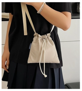 Detail of minimalist beige nylon crossbody bag featuring a blue NINGNING logo woven label