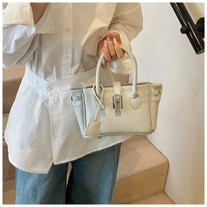 Close-up of litchi grain leather texture and metallic turn-lock on the cream bucket bag