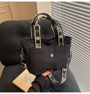 Detail der schwarzen Nylontasche mit floralem Gurt auf einem grauen Sessel