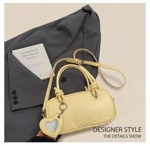 Détail du sac à main jaune pâle avec poignée nouée et breloque coeur sur un blazer gris