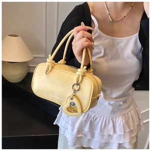 Détail d'un sac Boston jaune crème avec poignée nouée et breloque coeur sur modèle