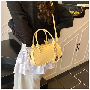 Détail d'un sac polochon en cuir jaune avec poignée nouée et breloque en forme de cœur