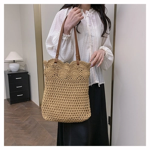 Detail of hollow woven straw tote bag with brown leather straps and rivet reinforcement