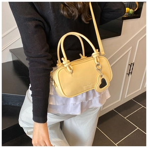 Détail du sac bandoulière jaune avec poignée nouée et breloque coeur sur fond noir et blanc