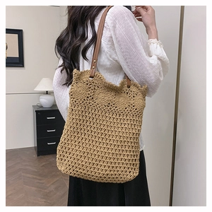 Detail of woven straw tote bag with crochet flower trim and brown leather handles