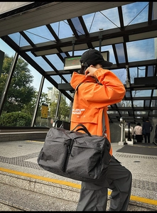 Détail du sac de voyage à carreaux gris foncé avec poignées en cuir et poches zippées
