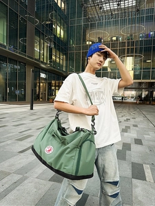Large grey-green nylon tote bag with shoulder strap worn by a model in a city setting