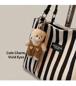Gros plan d'un pendentif ours en peluche avec salopette en velours sur un sac rayé
