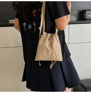 Detail of khaki nylon bucket bag showing drawstring closure and adjustable strap on model