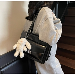 Détail d'un sac messager noir en cuir PU brillant avec un pendentif lapin en peluche
