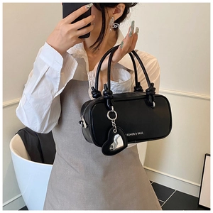 Détail du sac à main en cuir noir avec poignées nouées et breloque miroir en forme de cœur