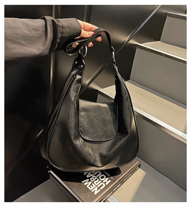 Close-up of black retro crescent tote bag with premium leather texture on urban books