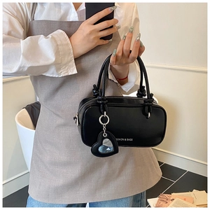 Détail du sac bandoulière noir avec poignée nouée et breloque cœur porté par un mannequin