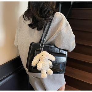 Détail d'une besace noire en similicuir avec un lapin en peluche blanc sur un mannequin
