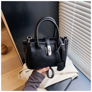 Detail of black pebbled leather handbag featuring silver metal twist lock and dual handles