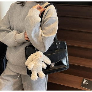 Détail d'un sac bandoulière carré en similicuir noir brillant avec un lapin en peluche