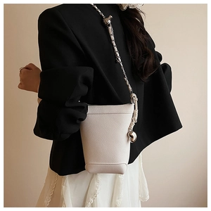 Détail du sac seau en cuir blanc avec chaîne en métal argenté et nœud à billes