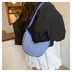 Detail view of a blue plaid canvas crescent bag with a striped wide shoulder strap