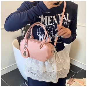 Détail du sac bandoulière rose avec poignées nouées et breloque en forme de cœur