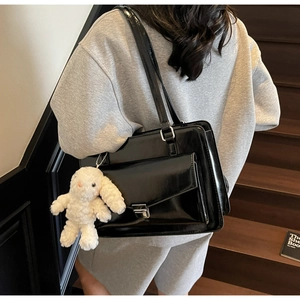 Détail d'un sac à main noir brillant avec fermoir argenté et breloque lapin en peluche