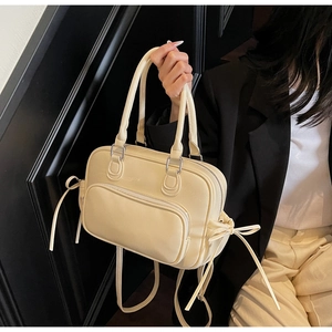 Detail of cream Boston bag with bow accents and adjustable strap shown on model